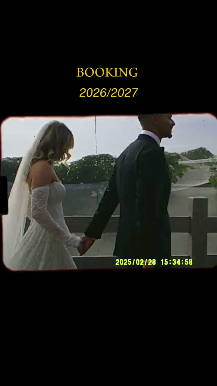 A bride and groom kissing during their outdoor wedding ceremony, with guests smiling and clapping in the background.