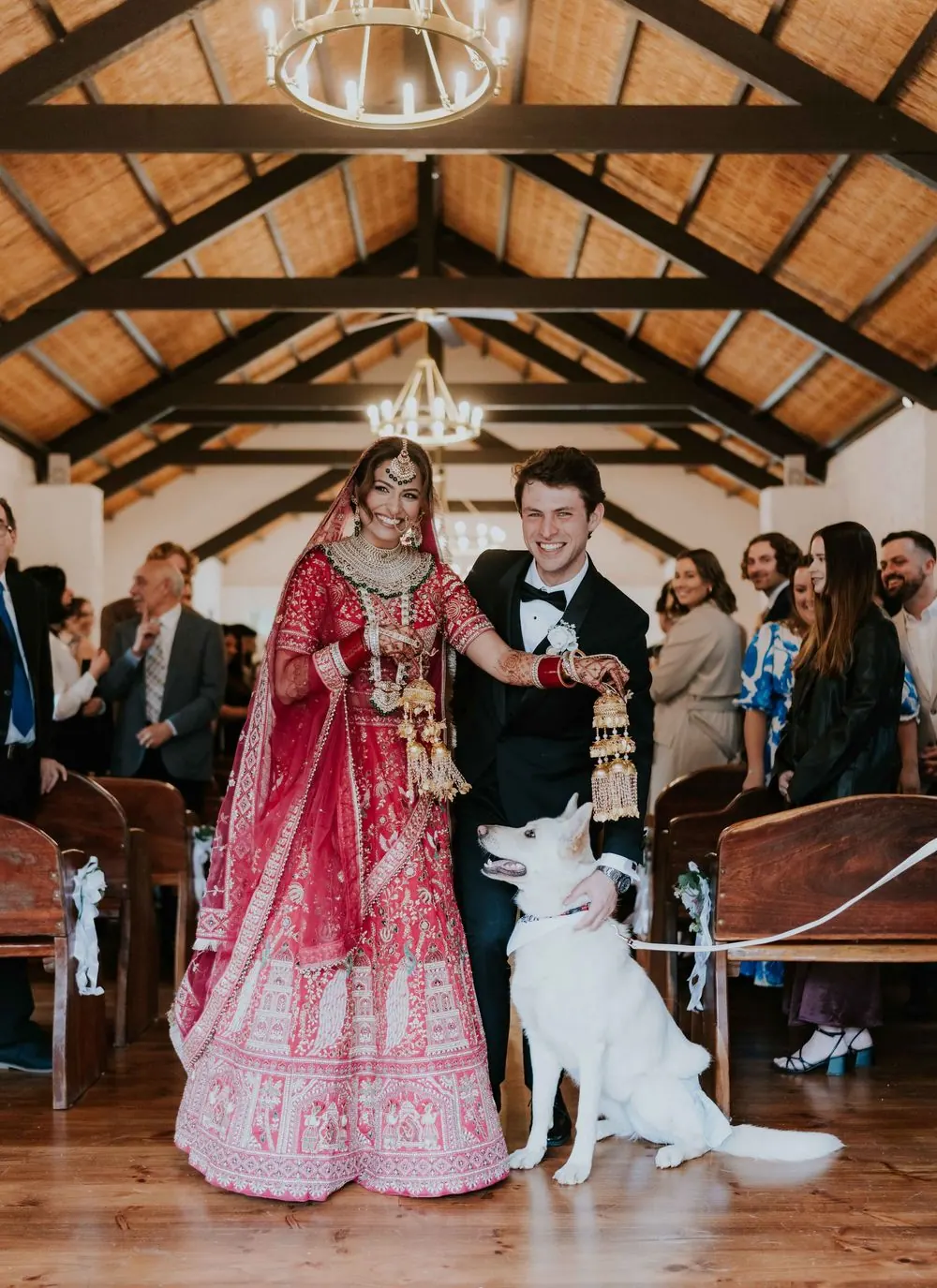A newly married couple in traditional and formal wedding attire walking with their dog.