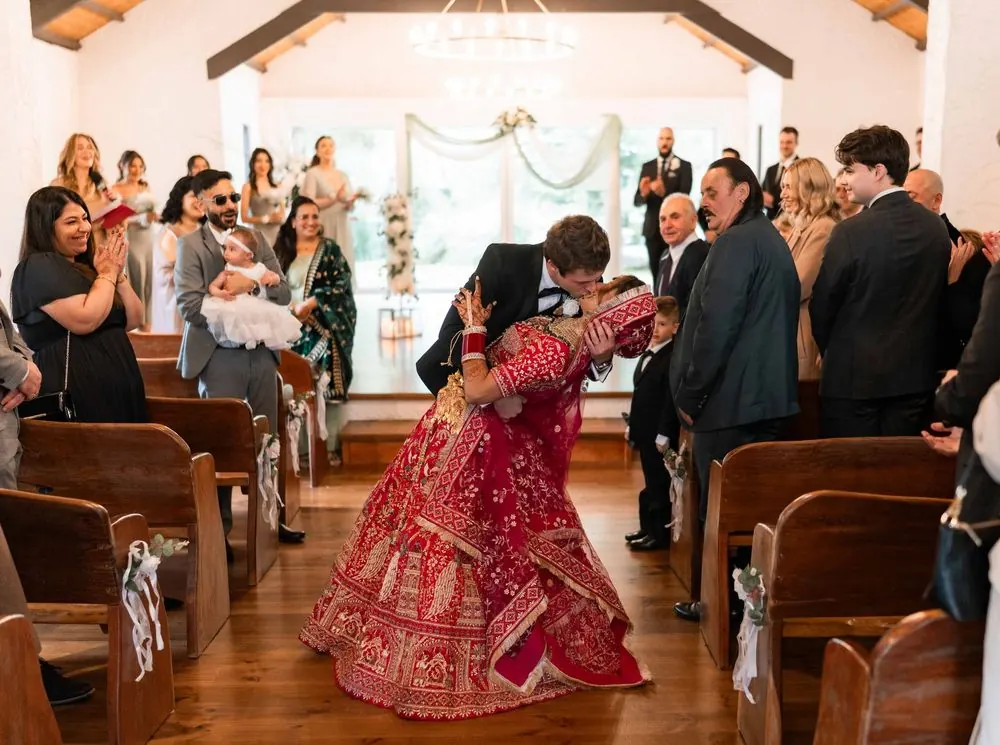 Newlyweds sharing a celebratory dip and kiss between rows of wedding guests.