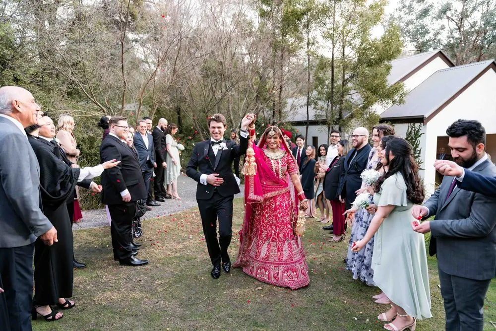 A newly married couple smiling as guests shower them with flower petals.