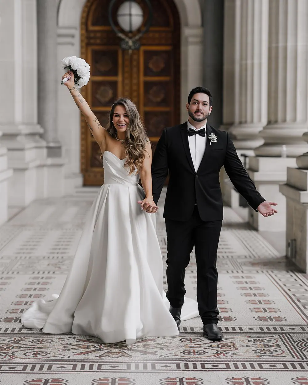 Newlyweds walking hand in hand outside a grand Melbourne building after their ceremony.